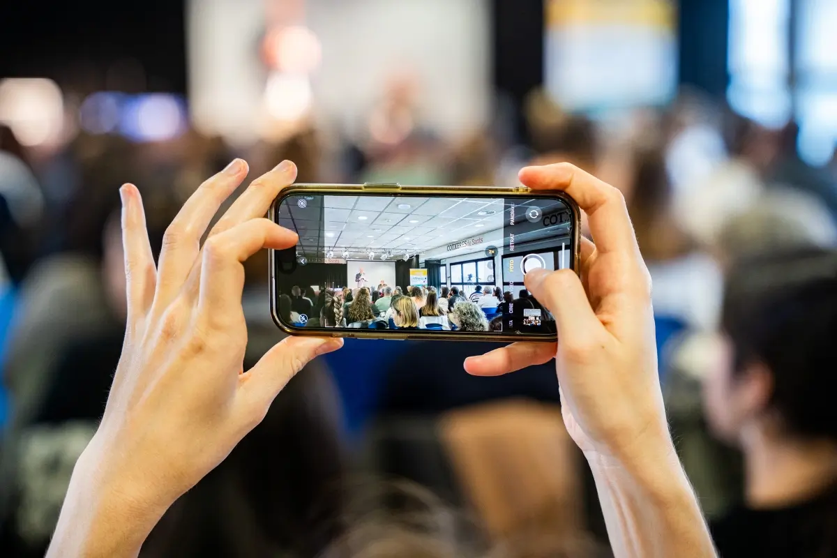 Foto de las manos de una persona haciendo una foto de la conferencia con su teléfono móvil